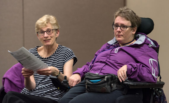 Une femme qui tient une liste est assise à côté d’une femme dans un fauteuil roulant